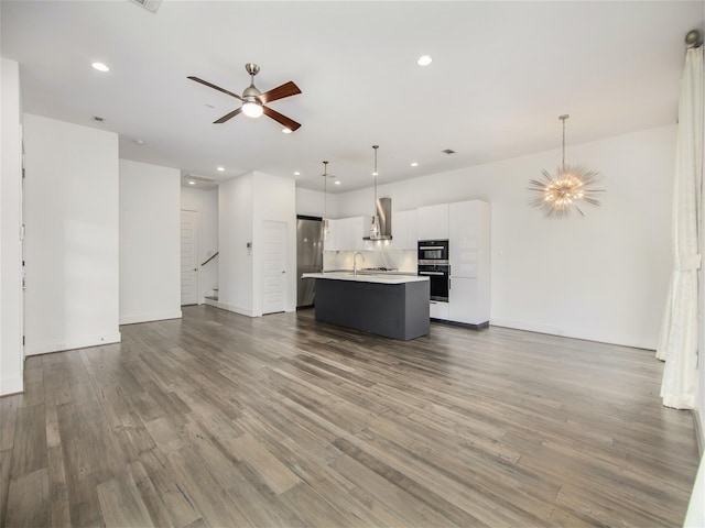 kitchen featuring pendant lighting, white cabinetry, backsplash, a center island with sink, and wall chimney range hood