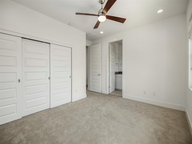 unfurnished bedroom with ensuite bath, light colored carpet, a closet, and ceiling fan