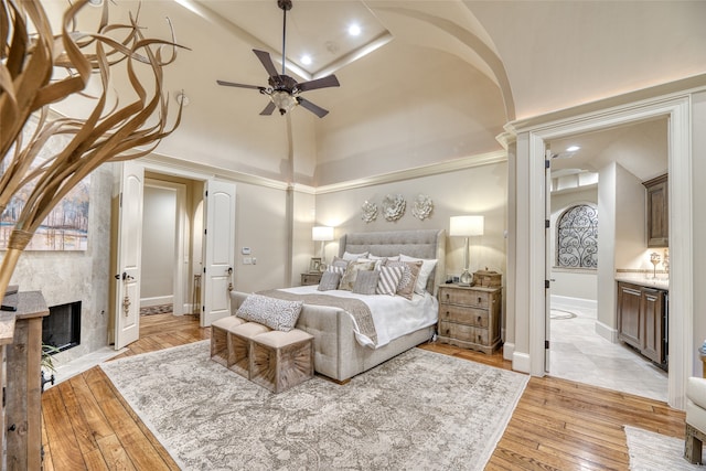 bedroom featuring light hardwood / wood-style floors, ceiling fan, a high ceiling, ensuite bath, and a high end fireplace