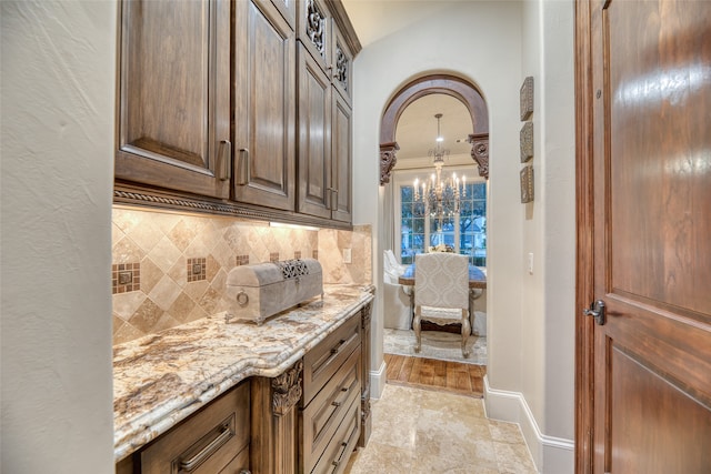 interior space with tasteful backsplash, light stone countertops, an inviting chandelier, and crown molding