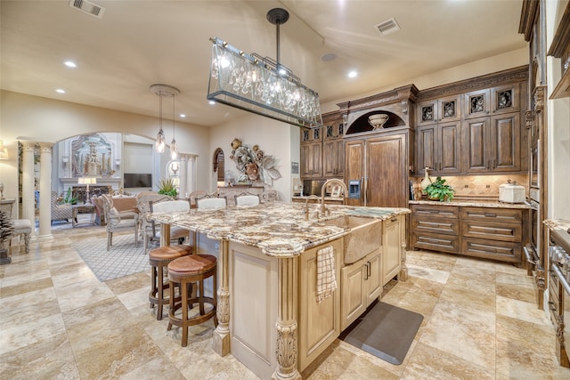 kitchen with a spacious island, pendant lighting, a breakfast bar, sink, and decorative columns