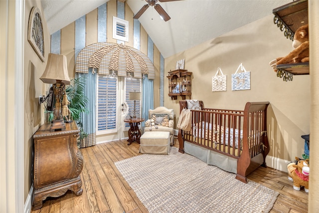 bedroom with ceiling fan, a crib, hardwood / wood-style flooring, a textured ceiling, and high vaulted ceiling