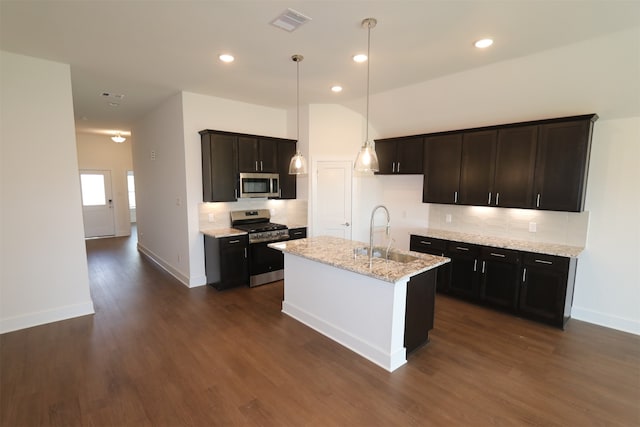 kitchen featuring light stone countertops, sink, dark hardwood / wood-style flooring, stainless steel appliances, and a kitchen island with sink