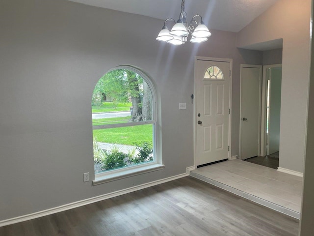 foyer with lofted ceiling, baseboards, a chandelier, and wood finished floors