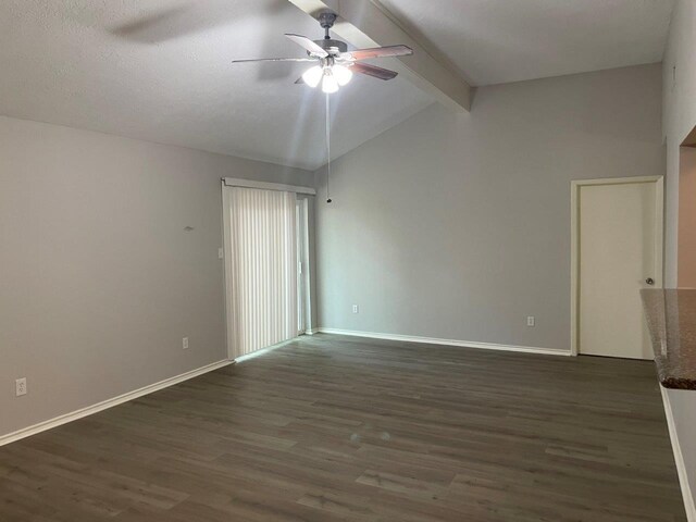 spare room featuring lofted ceiling with beams, dark wood-type flooring, a ceiling fan, and baseboards