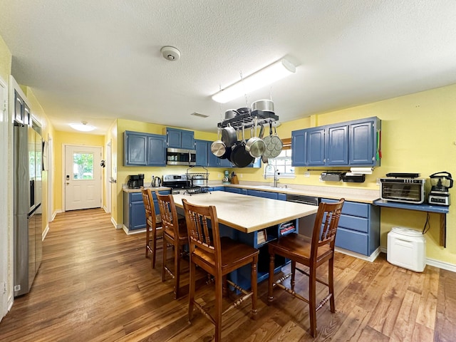 kitchen with appliances with stainless steel finishes, sink, light wood-type flooring, a textured ceiling, and blue cabinetry