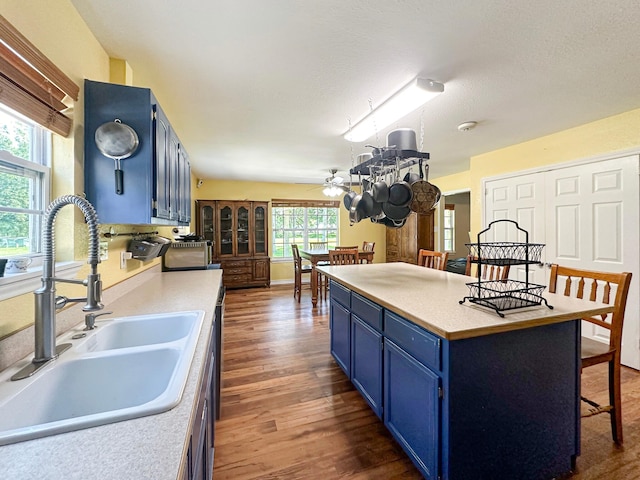 kitchen with ceiling fan, blue cabinets, hardwood / wood-style floors, sink, and a textured ceiling