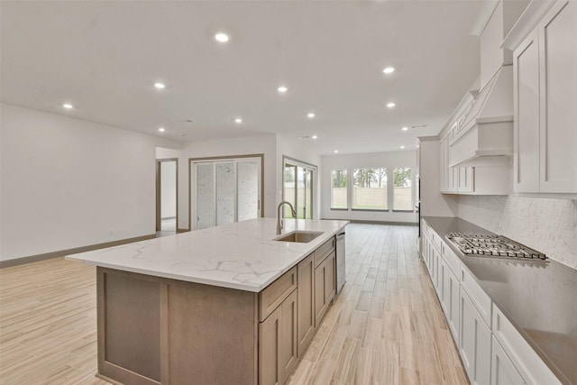 kitchen featuring light stone counters, stainless steel appliances, sink, a large island with sink, and white cabinetry