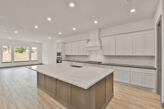 kitchen featuring premium range hood, white cabinetry, a large island, and sink