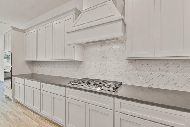 kitchen featuring light wood-type flooring, custom range hood, tasteful backsplash, white cabinetry, and stainless steel appliances