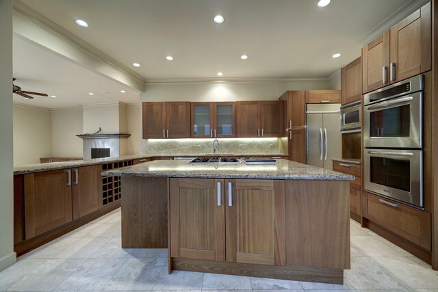 kitchen with ceiling fan, built in appliances, decorative backsplash, a center island, and light stone counters