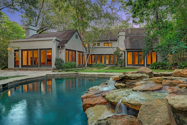 pool at dusk with pool water feature and a patio area