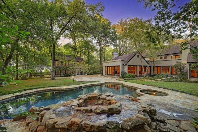 pool at dusk with a patio, an in ground hot tub, and a lawn