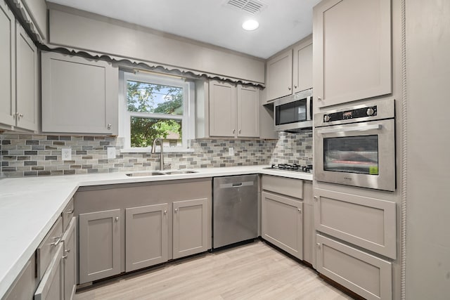 kitchen with decorative backsplash, appliances with stainless steel finishes, gray cabinetry, sink, and light hardwood / wood-style flooring