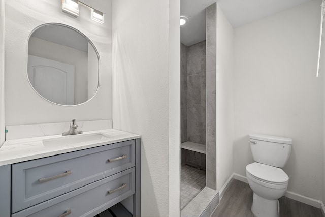 bathroom with a tile shower, hardwood / wood-style floors, vanity, and toilet