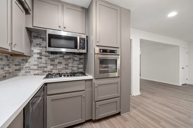 kitchen featuring backsplash, stainless steel appliances, gray cabinetry, and light hardwood / wood-style floors