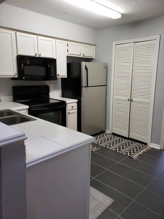 kitchen with a textured ceiling, white cabinets, black appliances, dark tile patterned floors, and sink