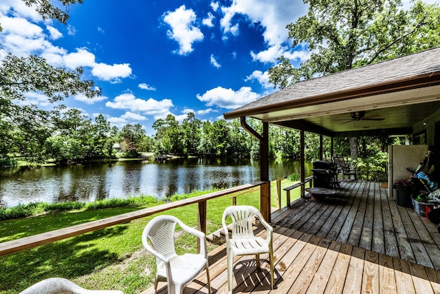 wooden terrace with a water view, ceiling fan, grilling area, and a lawn