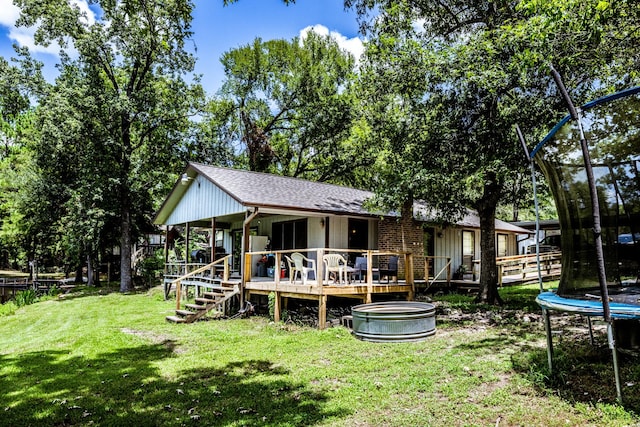 back of property with stairs, a yard, roof with shingles, a wooden deck, and a trampoline