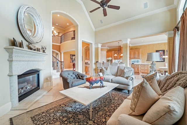 living room with light tile patterned floors, crown molding, ceiling fan with notable chandelier, ornate columns, and high vaulted ceiling