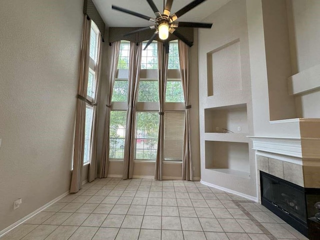 interior space with built in shelves, ceiling fan, a tiled fireplace, and light tile patterned flooring