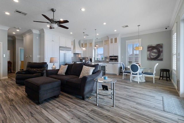 living room with ceiling fan, ornamental molding, sink, wine cooler, and light hardwood / wood-style flooring