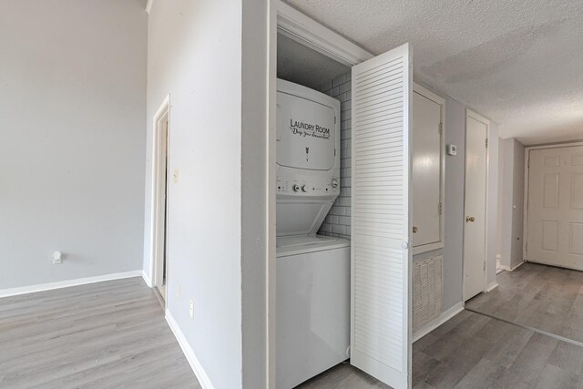 laundry area featuring a textured ceiling, stacked washer and clothes dryer, and light wood-type flooring