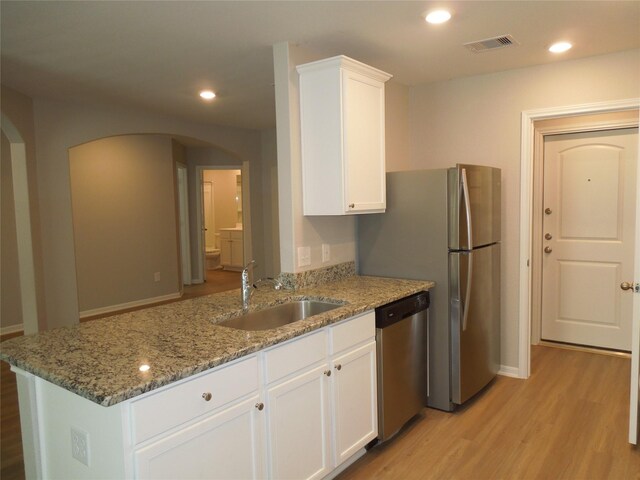 kitchen with stainless steel dishwasher, white cabinetry, stone counters, light wood-type flooring, and sink