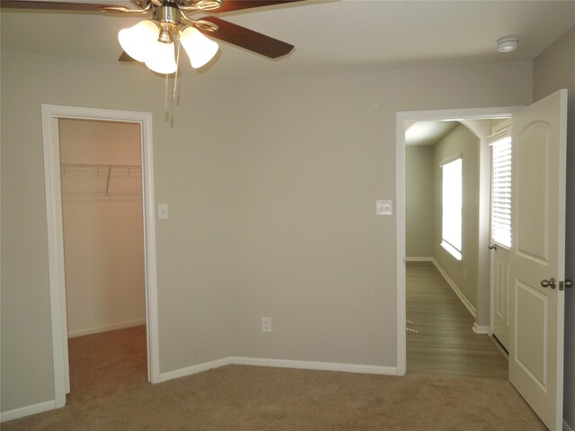 unfurnished bedroom with a closet, carpet flooring, ceiling fan, and a spacious closet