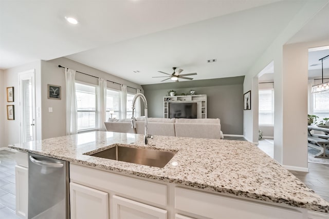 kitchen with stainless steel dishwasher, sink, light stone counters, and white cabinetry