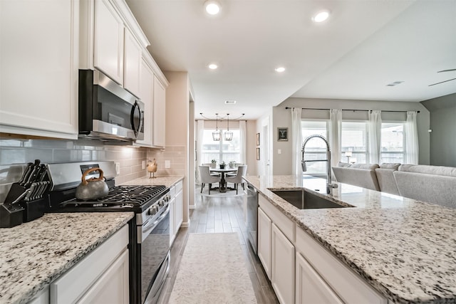 kitchen featuring stainless steel appliances, tasteful backsplash, light stone countertops, white cabinets, and sink