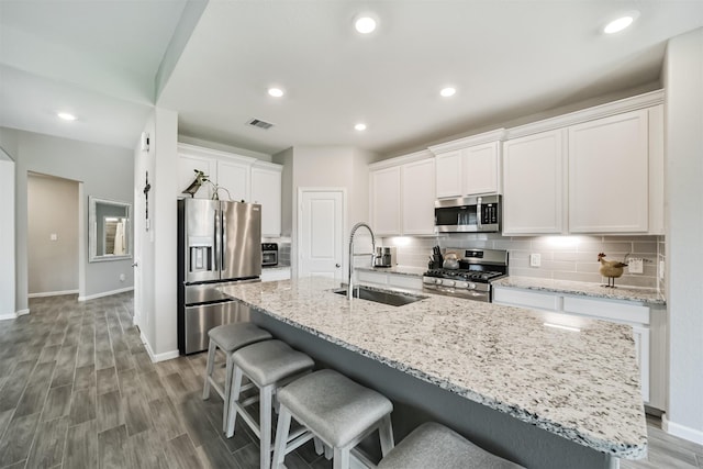 kitchen featuring an island with sink, sink, stainless steel appliances, and white cabinetry