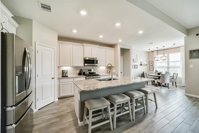 kitchen featuring white cabinetry, a kitchen bar, a center island with sink, stainless steel appliances, and sink