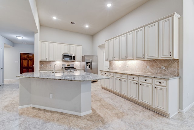 kitchen featuring tasteful backsplash, stainless steel appliances, light stone countertops, and a kitchen island with sink