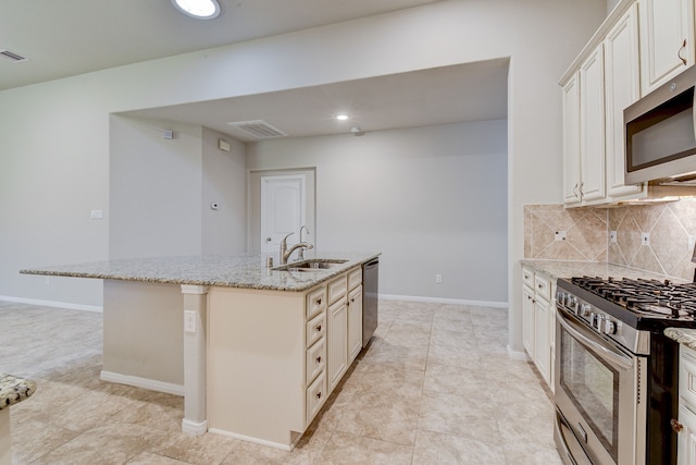 kitchen featuring sink, appliances with stainless steel finishes, light stone countertops, a kitchen island with sink, and decorative backsplash