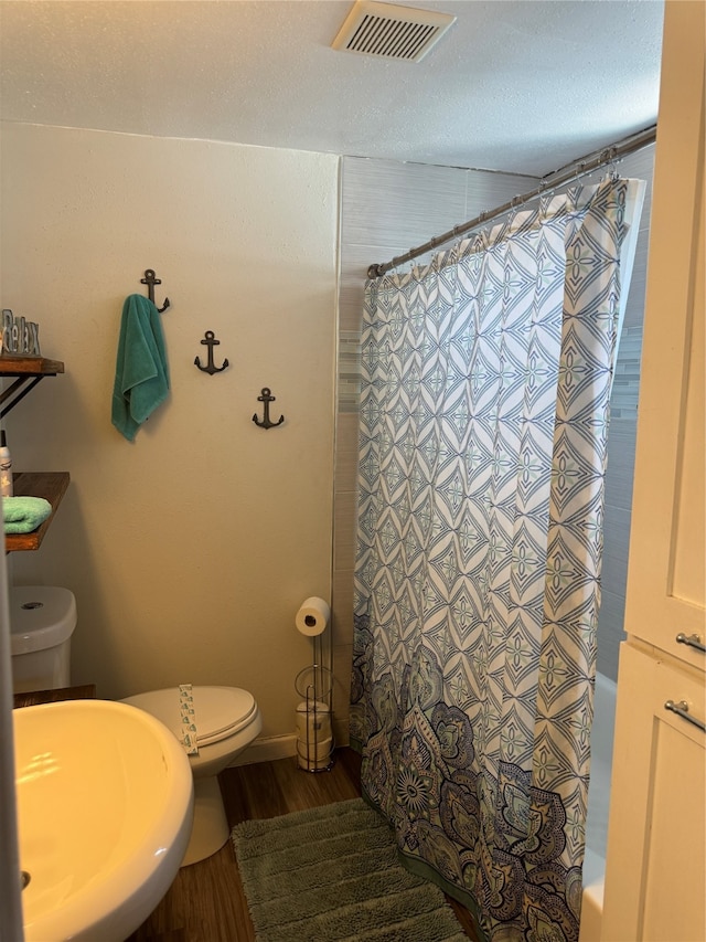 full bathroom featuring sink, shower / bathtub combination with curtain, a textured ceiling, toilet, and hardwood / wood-style flooring