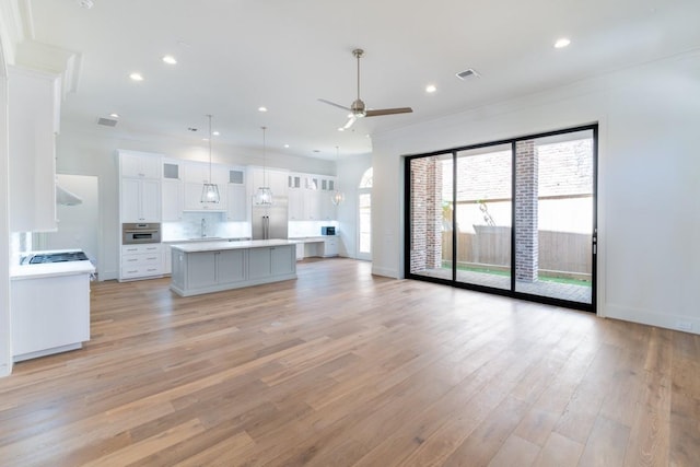 unfurnished living room with ceiling fan, sink, ornamental molding, and light wood-type flooring