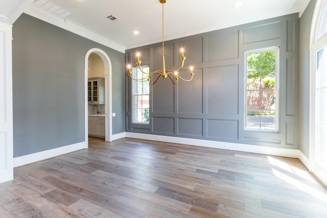 unfurnished dining area with wood-type flooring, a notable chandelier, sink, and ornamental molding