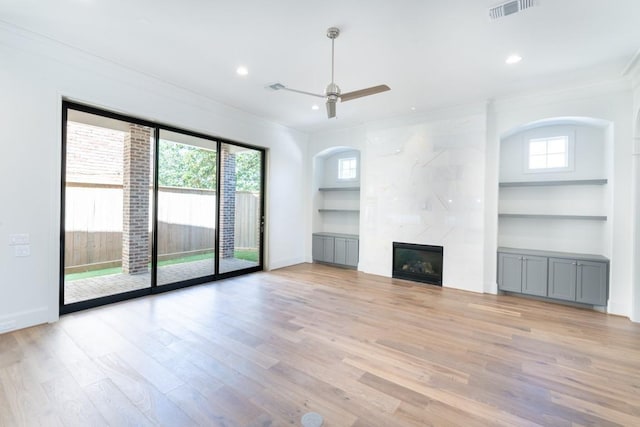 unfurnished living room featuring ceiling fan, a premium fireplace, ornamental molding, light hardwood / wood-style flooring, and built in shelves