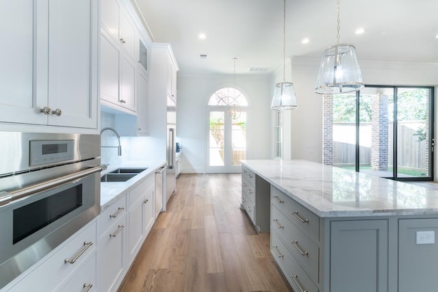 kitchen with decorative light fixtures, a kitchen island, sink, stainless steel oven, and white cabinets