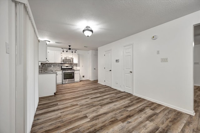 kitchen with white cabinets, backsplash, stainless steel appliances, a textured ceiling, and hardwood / wood-style floors