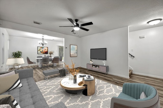 living room with a textured ceiling, ceiling fan with notable chandelier, and dark wood-type flooring