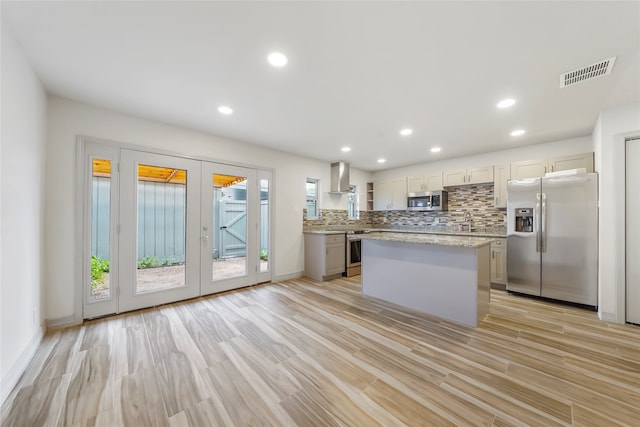 kitchen with appliances with stainless steel finishes, tasteful backsplash, french doors, a kitchen island, and wall chimney exhaust hood