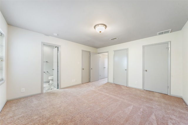 unfurnished bedroom featuring light colored carpet and ensuite bath