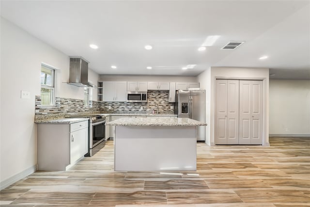 kitchen featuring stainless steel appliances, backsplash, light stone countertops, a center island, and wall chimney exhaust hood