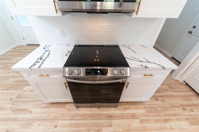 kitchen featuring electric stove, light wood-style flooring, light stone counters, white cabinetry, and backsplash