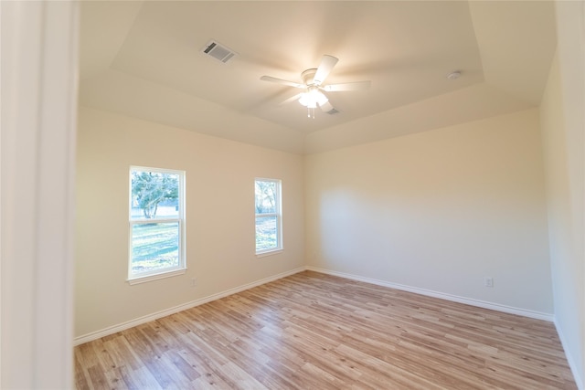 unfurnished room featuring a tray ceiling, visible vents, ceiling fan, and light wood-style flooring