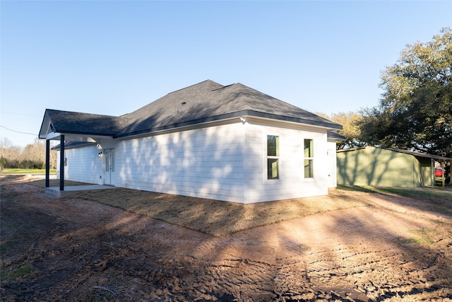 view of property exterior with roof with shingles and a patio