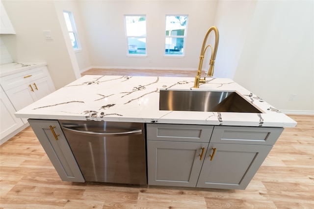 kitchen featuring light wood finished floors, gray cabinets, stainless steel dishwasher, a sink, and light stone countertops