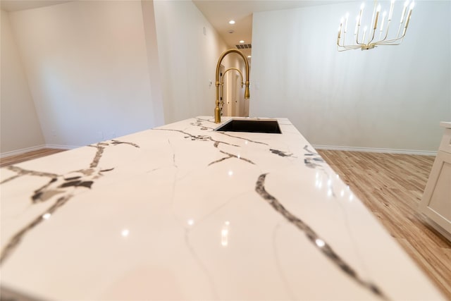 interior details with baseboards, light wood-style flooring, a sink, light stone countertops, and a notable chandelier